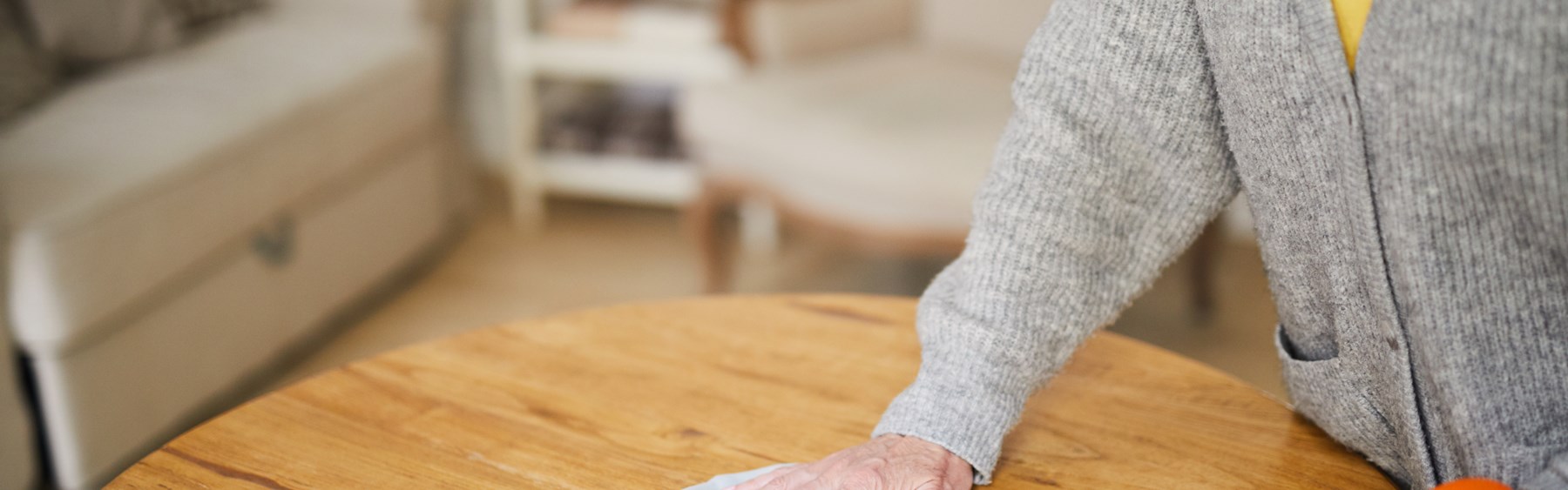 Ældre person tørrer et træbord bord af med en køkkenklud. 