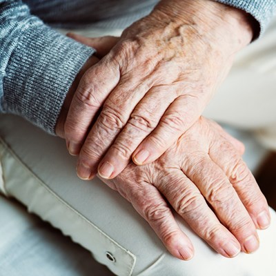 Ældre person sidder med hænderne foldet over hinanden.