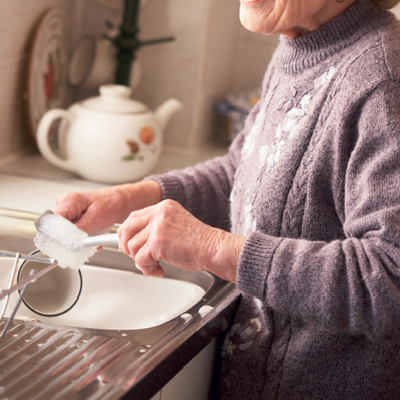 Ældre dame vasker en kop op. Hun smiler og er glad.